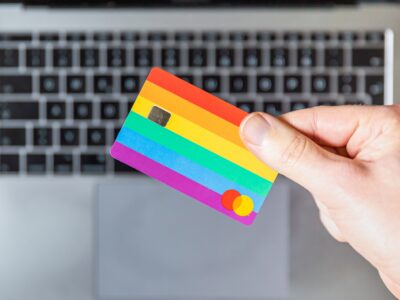 An LGBTQ flag debit card held over a laptop