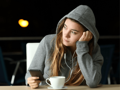 A teen girl listening to music and holding a phone with a cup of coffee.